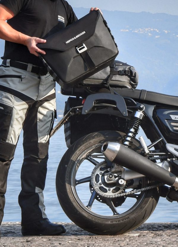 Mann der eine schwarze Motorradtasche an seinem Motorrad befestigt.